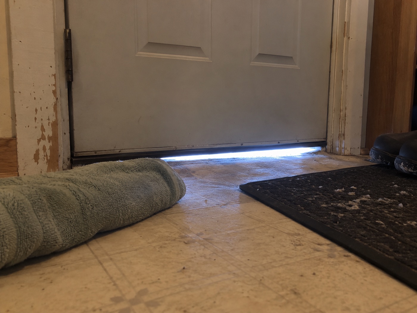 Daylight showing under the bottom of a front door, a rolled towel on the floor in front of it.